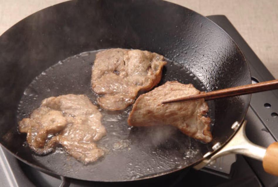 Marinated beef slices sizzling in a cast-iron skillet, developing a caramelized crust.