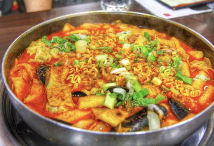 Topping and serving Army Stew Korean with tofu, cheese, mushrooms, and green onions.