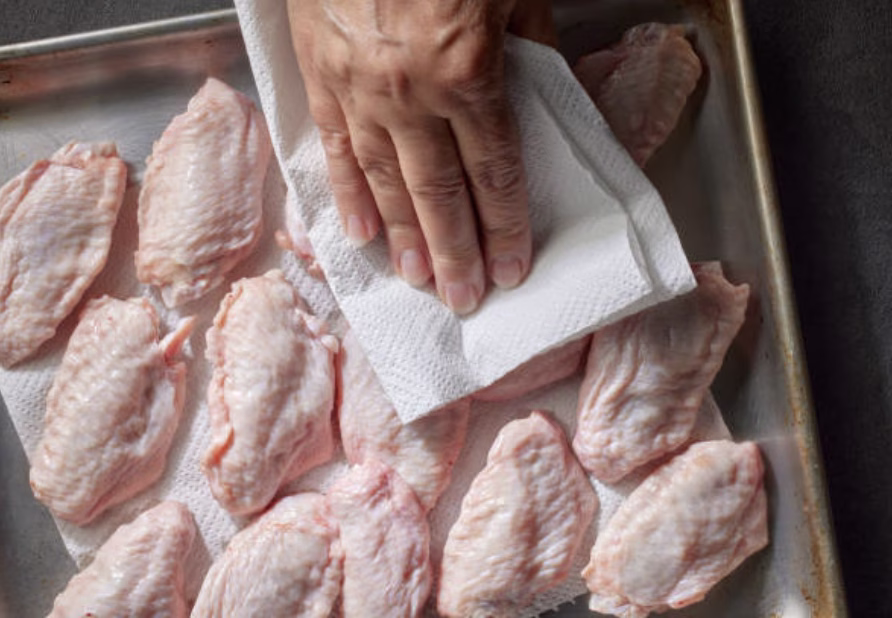 Raw chicken pieces being patted dry with paper towels in preparation for Korean fried chicken.