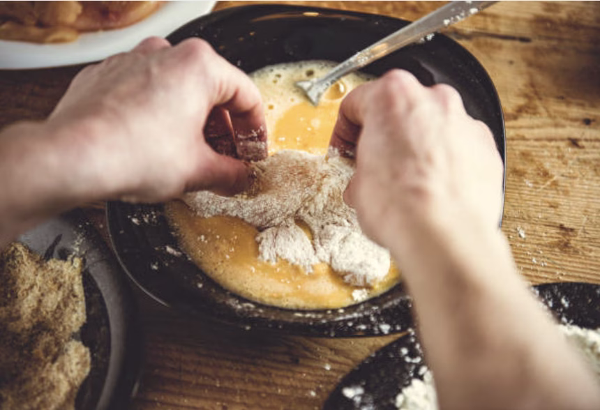 Chicken pieces being dipped into batter, ensuring an even coating for Korean fried chicken.