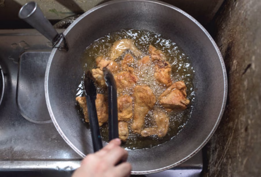 Chicken pieces frying in hot oil during the double-fry process for Korean fried chicken.