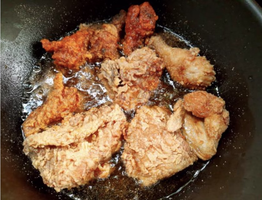 Fully cooked Korean fried chicken pieces being tossed in spicy sauce before serving.
