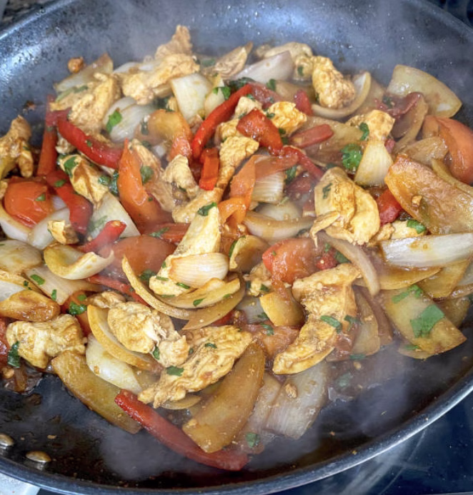 Adding shredded rotisserie chicken to japchae vegetable mix in a skillet