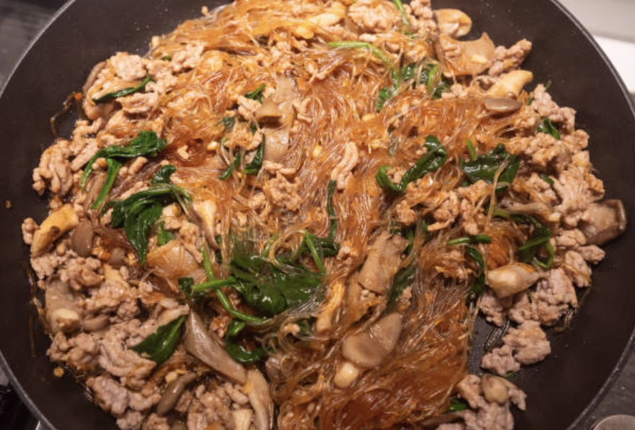 Tossing noodles, chicken, and veggies with japchae sauce in a large skillet