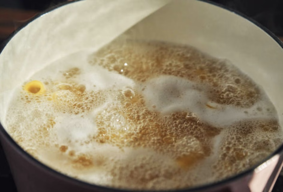 Chicken broth boiling in a pot for mandu guk preparation