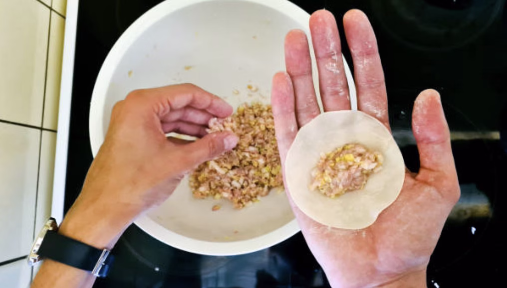Filling mandu wrappers with a spoonful of turkey and vegetable mix