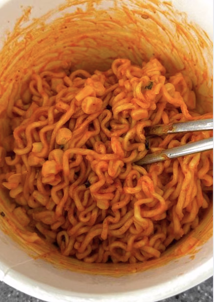 Tossing hot ramen noodles with shredded buldak chicken and sauce